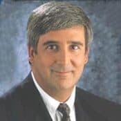 Man in suit with gray hair smiling.