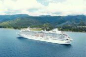 Cruise ship sailing near lush green mountains.