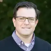 Man with glasses, wearing checkered shirt, smiling.