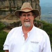 Man with hat smiling outdoors near rock formation.