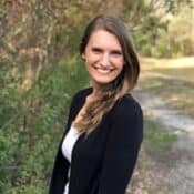 Smiling woman standing on a wooded path.