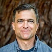 Man smiling in front of tree background.
