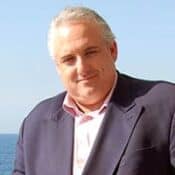 Man smiling in suit by the sea.