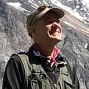 Man smiling in mountain landscape background.