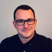 Man wearing glasses, smiling, with short hair.