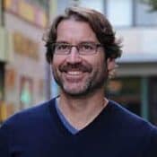 Smiling man with glasses in urban setting.