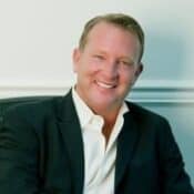 Smiling man in a suit, seated indoors.
