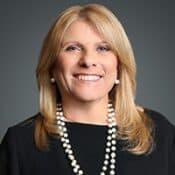 Smiling woman with long hair and pearls.