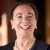 Smiling woman wearing pearls and dark outfit.