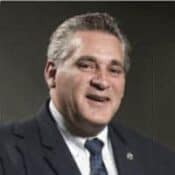 Man in suit smiling against dark background.