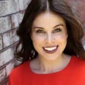 Smiling person in red near brick wall.
