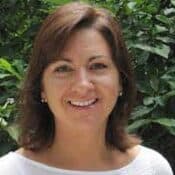 Smiling woman in front of green foliage.