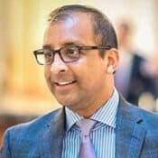 Man in glasses wearing suit and tie.