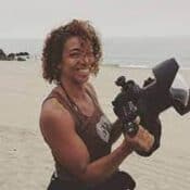 Smiling person holding camera on beach.