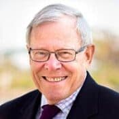 Elderly man smiling, wearing glasses and suit.